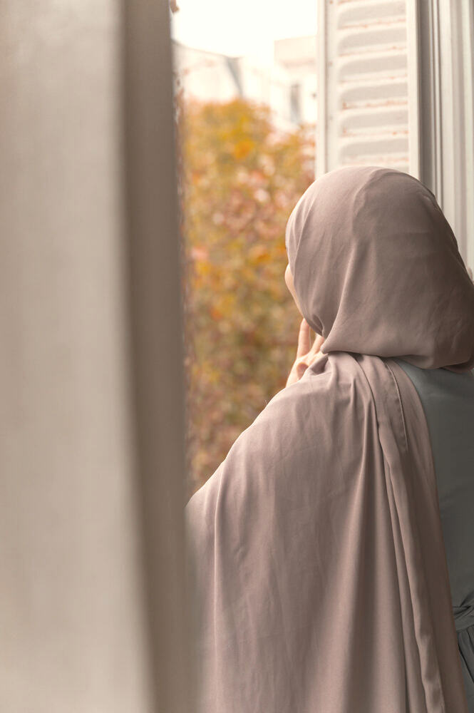 Ustadha Rahma à la fenêtre, devant un arbre d'automne