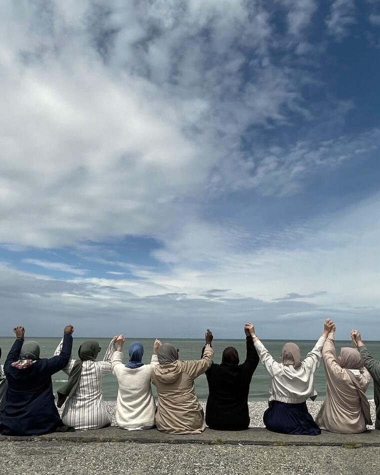 Des femmes de dos face à la mer, mains levées